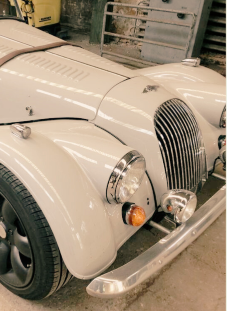 Ein klassischer, silberner Sportwagen mit runden Scheinwerfern und einem markanten Kühlergrill.