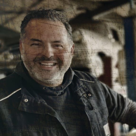 Lächelnder Mann in Arbeitskleidung in seiner Werkstatt.