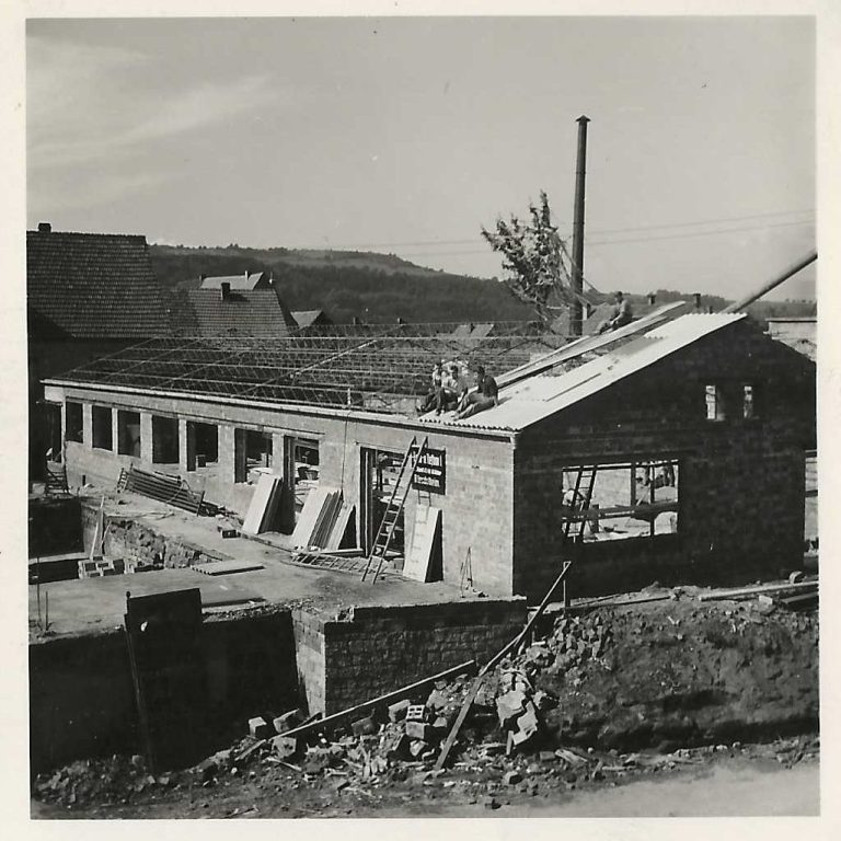 Blick auf ein altes einstöckiges Gebäude mit Holzplanken und einem Schornstein im Hintergrund aus den 1950er Jahren
