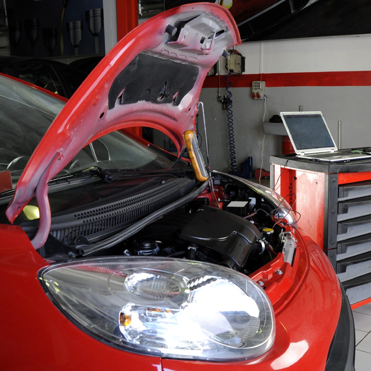 Roter PKW mit offenem Motorhaube in einer Werkstatt, Computer im Hintergrund.