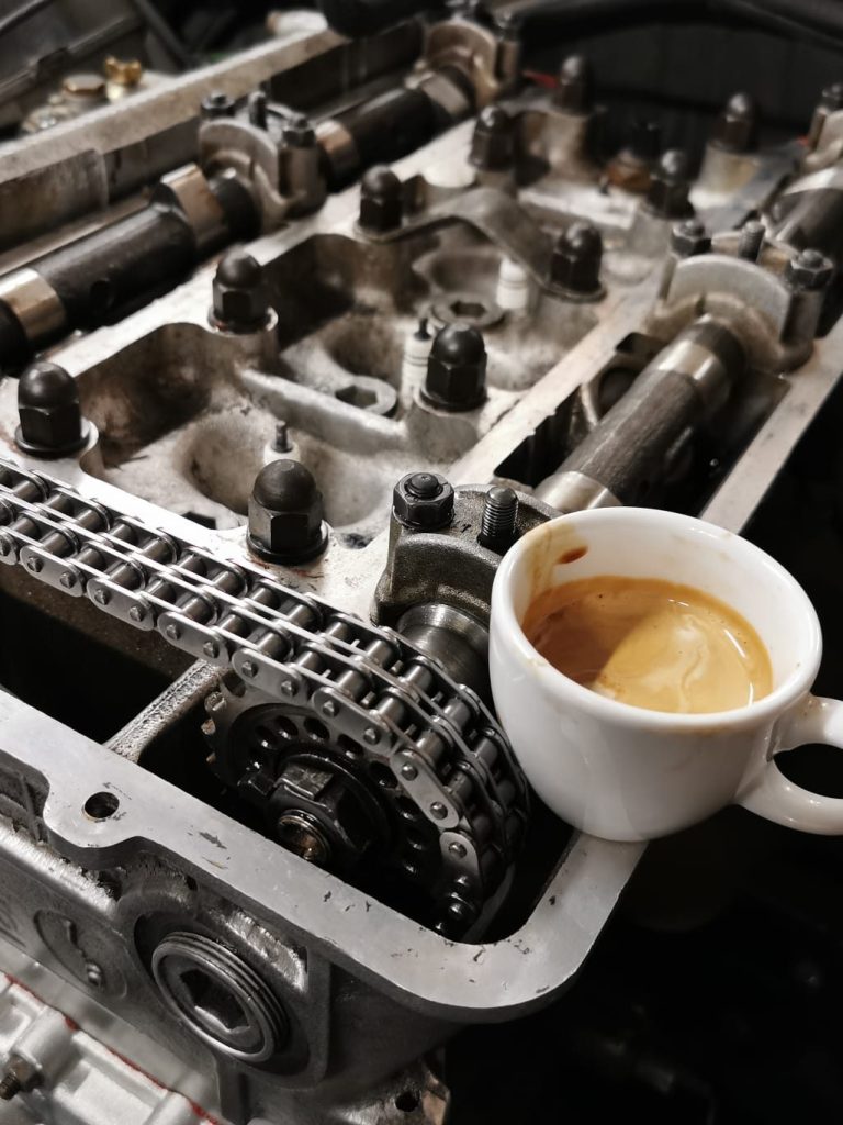 Eine Tasse italienischer Espresso steht auf einem offenen Motorblock mit sichtbarem Motorinnenteil.